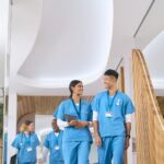 Multi Cultural Medical Team Wearing Scrubs Walking Along Corridor In Modern Hospital